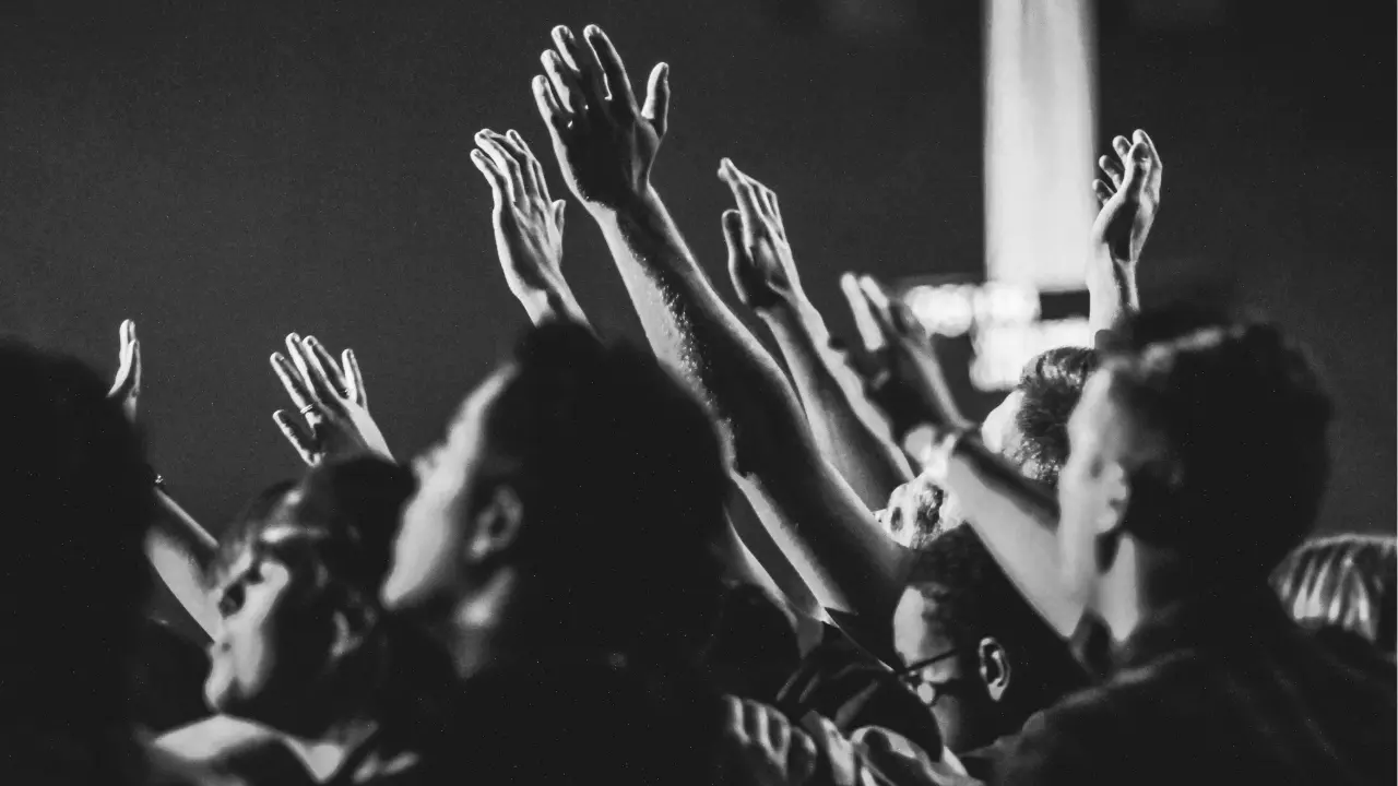 Ludzie z uniesionymi rękami w geście uwielbienia podczas nabożeństwa; czarno-biała fotografia.